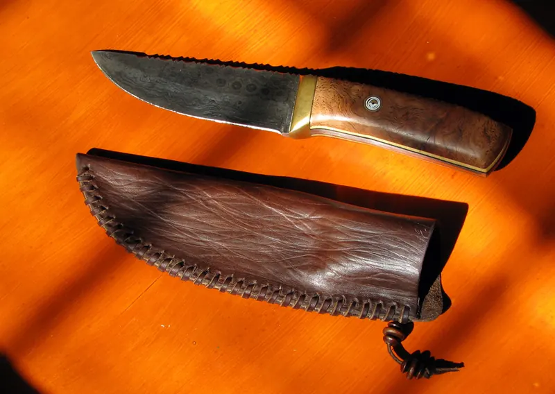Oak-burl handled knife and its brown leather sheath on the workbench