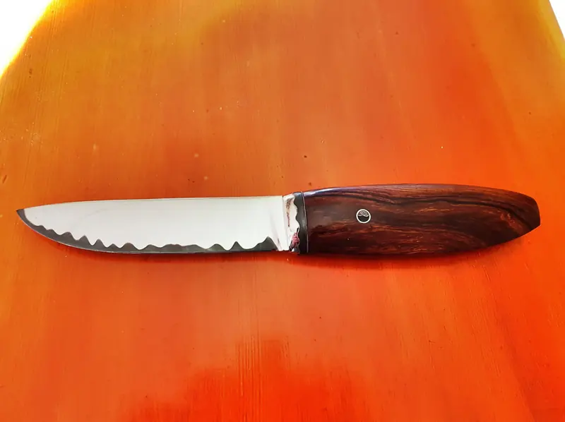 Finished serrated knife with a shaped wooden handle on the workbench