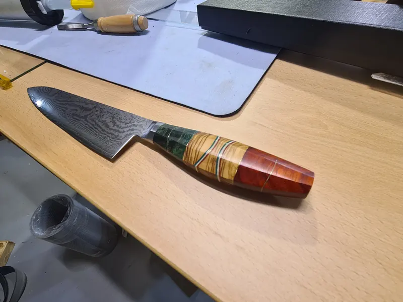 Finished kitchen knife with a patterned blade and green, striped and reddish handle sections