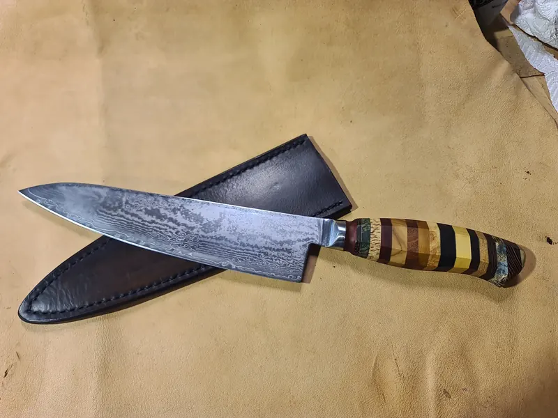 Striped-handled chef’s knife laid across its dark leather sheath