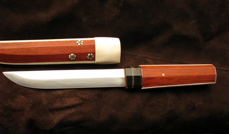 A knife partially drawn from its matching reddish wooden sheath with pale contrasting trim