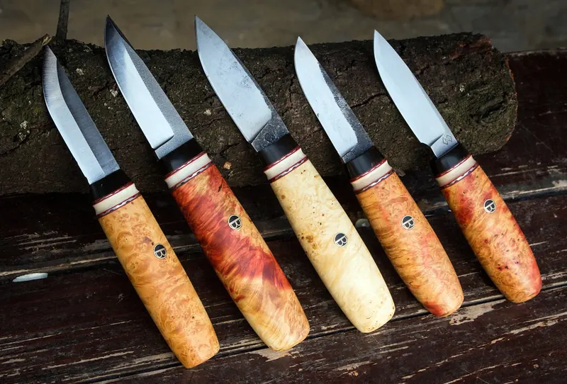 Five handmade knives with contrasting wooden handles arranged on weathered timber