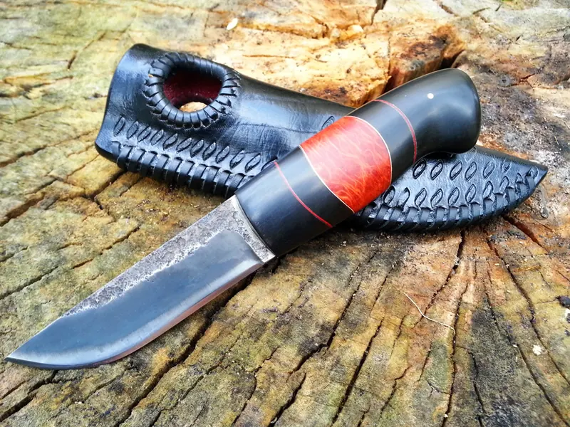 Knife with a black handle and red band beside a textured black sheath with red details