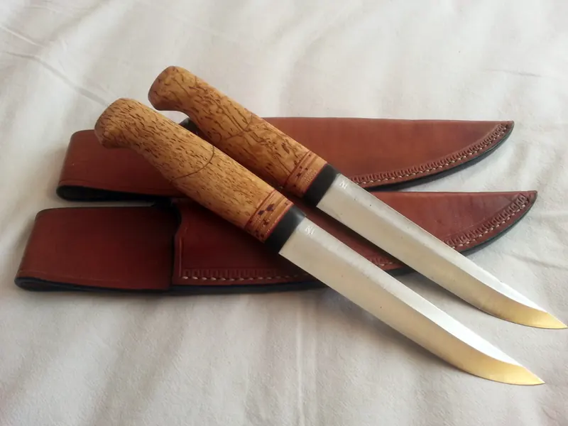Two slim knives with figured wooden handles beside their fitted brown leather sheaths