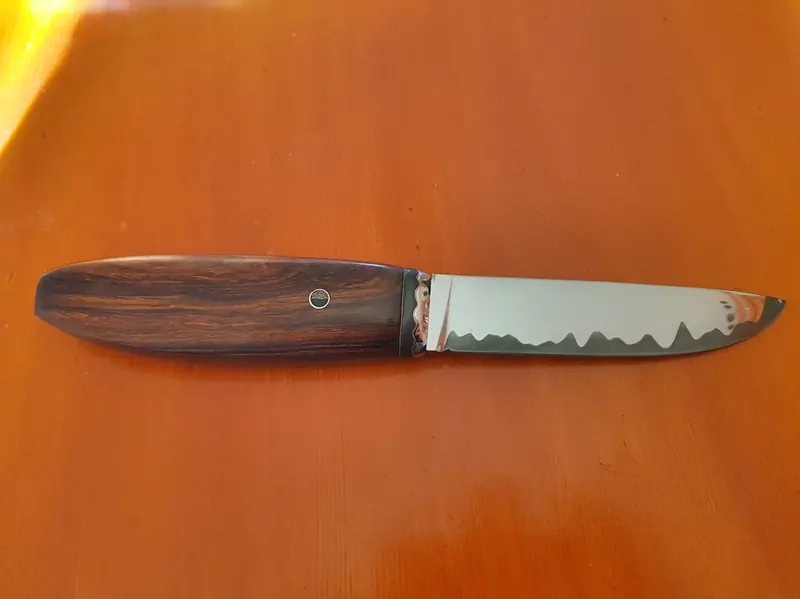 Finished knife with a wooden handle and decorative blade line, photographed on an orange work surface