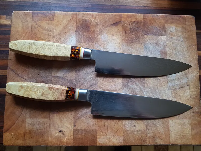 Two broad kitchen knives with pale, figured wooden handles photographed side by side